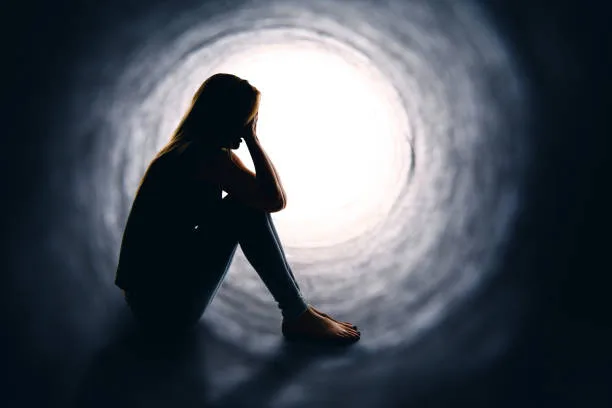 A depressed woman sitting alone is a dark tunnel with light at the other end.
